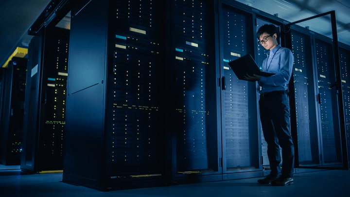 man holding laptop standing in control room representing how to get a data center technician job
