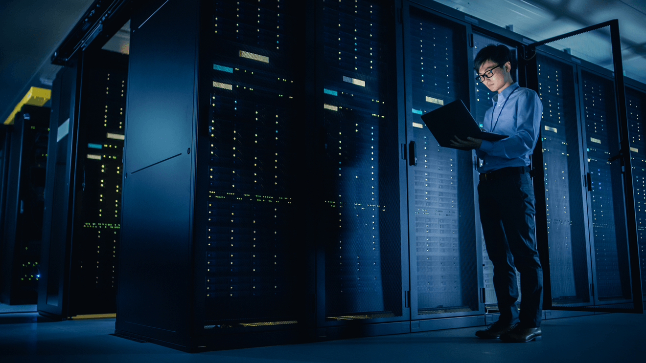 man holding laptop standing in control room representing how to get a data center technician job