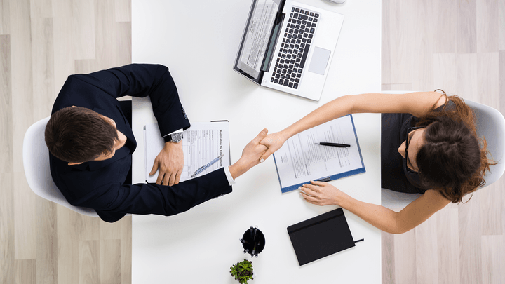 businessman and woman shaking hands with laptop on desk