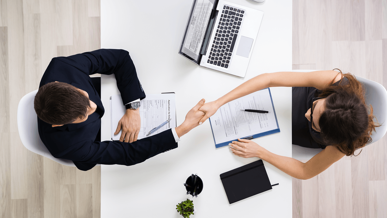 businessman and woman shaking hands with laptop on desk
